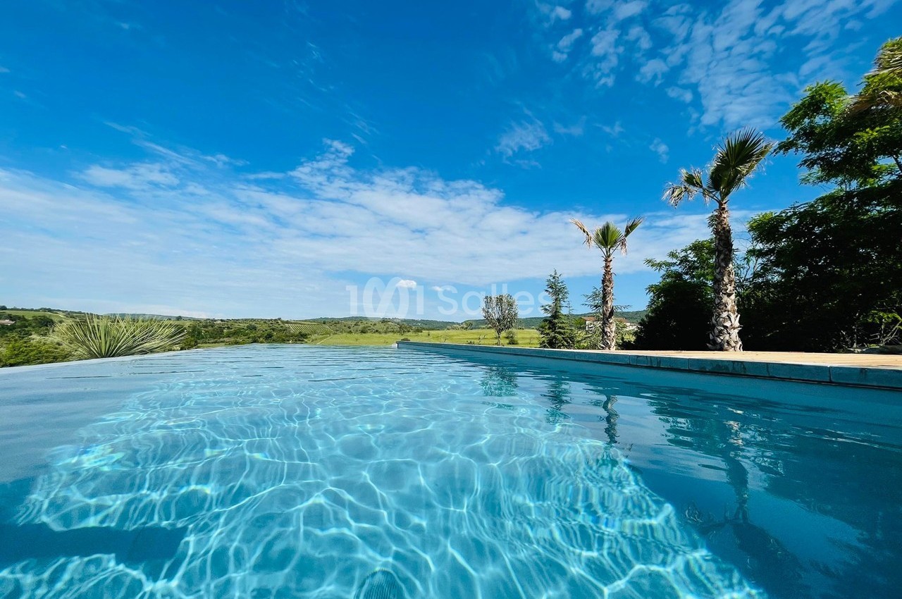 Piscine à débordement avec vue sur un paysage verdoyant sous un ciel bleu parsemé de nuages.