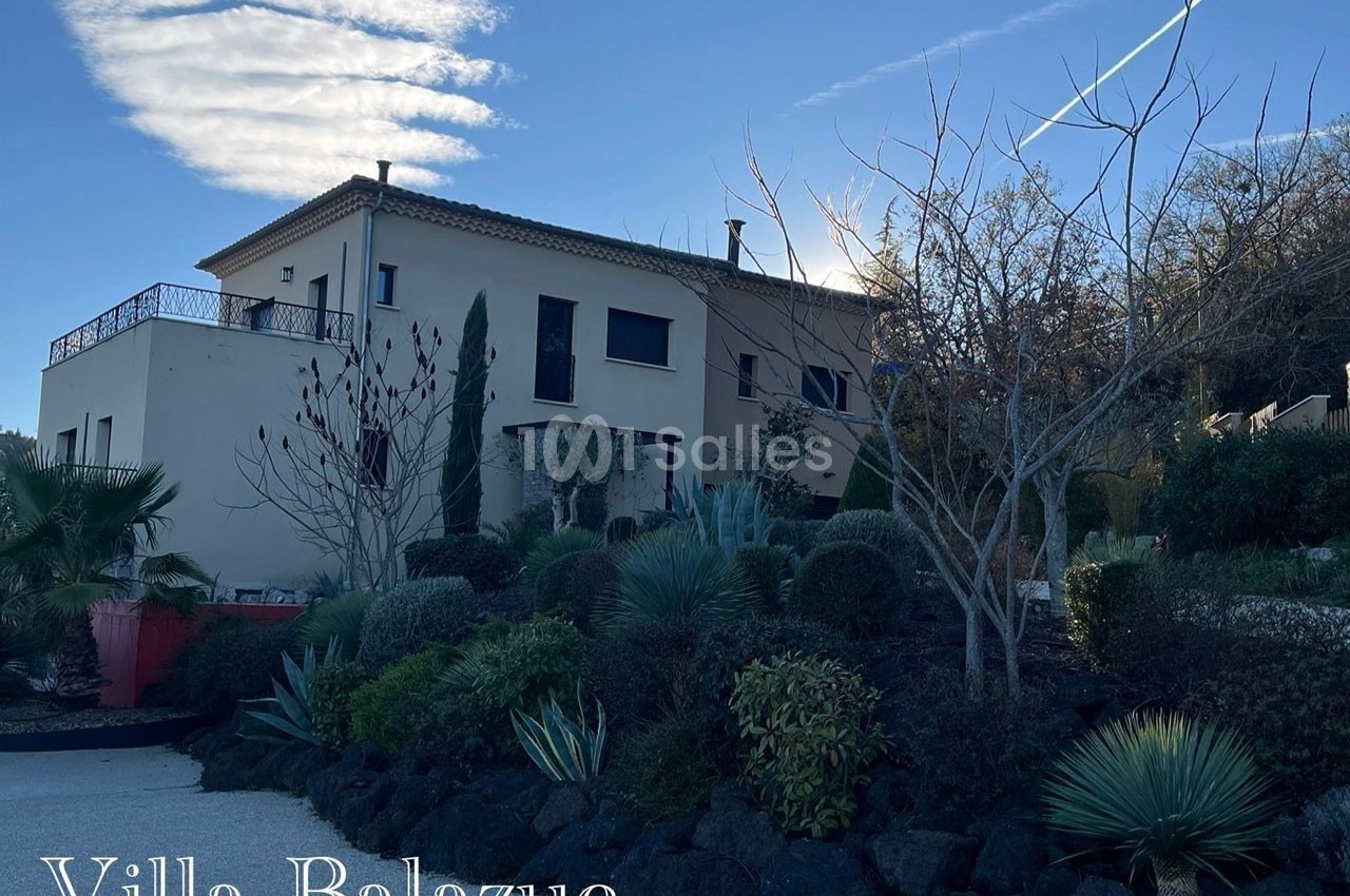 Vue d'une villa moderne entourée d'un jardin arboré et de végétation méditerranéenne sous un ciel dégagé.