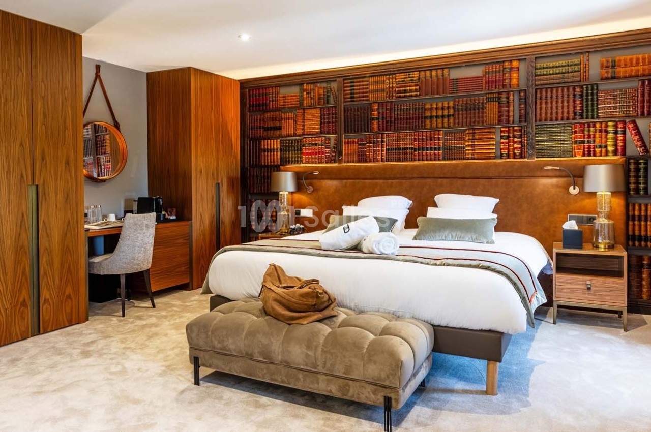 Chambre élégante avec lit double, étagères remplies de livres, bureau en bois et fauteuil capitonné devant le lit.