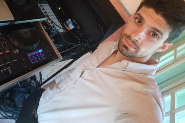 Homme en chemise claire près d'un équipement de DJ avec câbles et platines dans un espace intérieur lumineux.