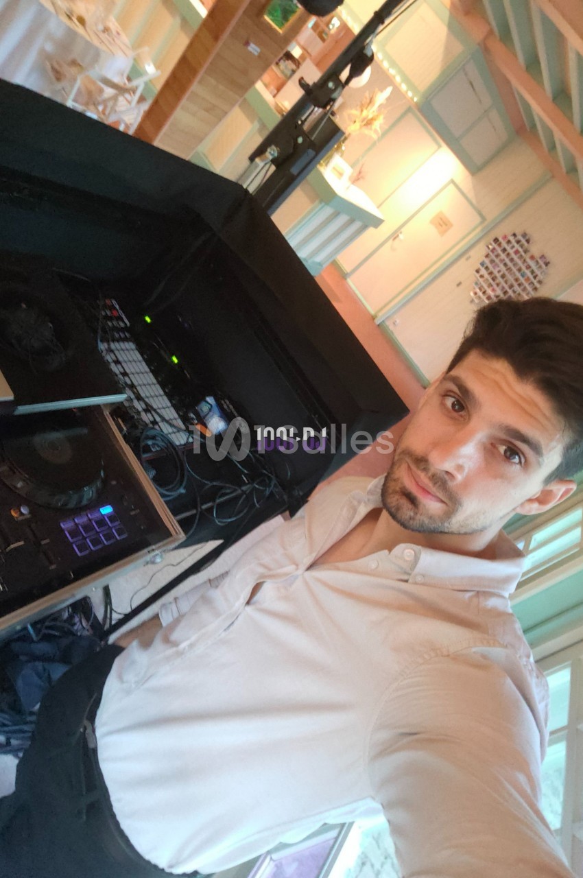 Un homme en chemise blanche se tient près d'une table de mixage dans un espace intérieur lumineux.