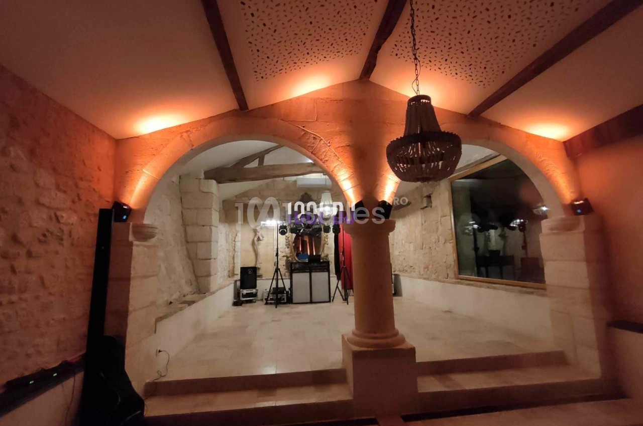 Salle voûtée en pierre avec éclairage tamisé, lustre suspendu et équipement audio installé au fond.