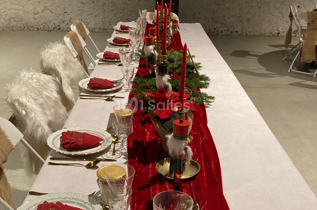 Table décorée pour un repas festif avec nappe rouge, bougies, poinsettias et assiettes dressées.