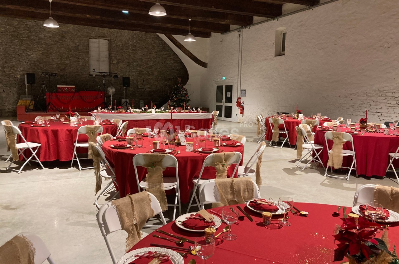 Salle de réception décorée pour un événement, avec des tables rondes dressées de nappes rouges et des chaises blanches.