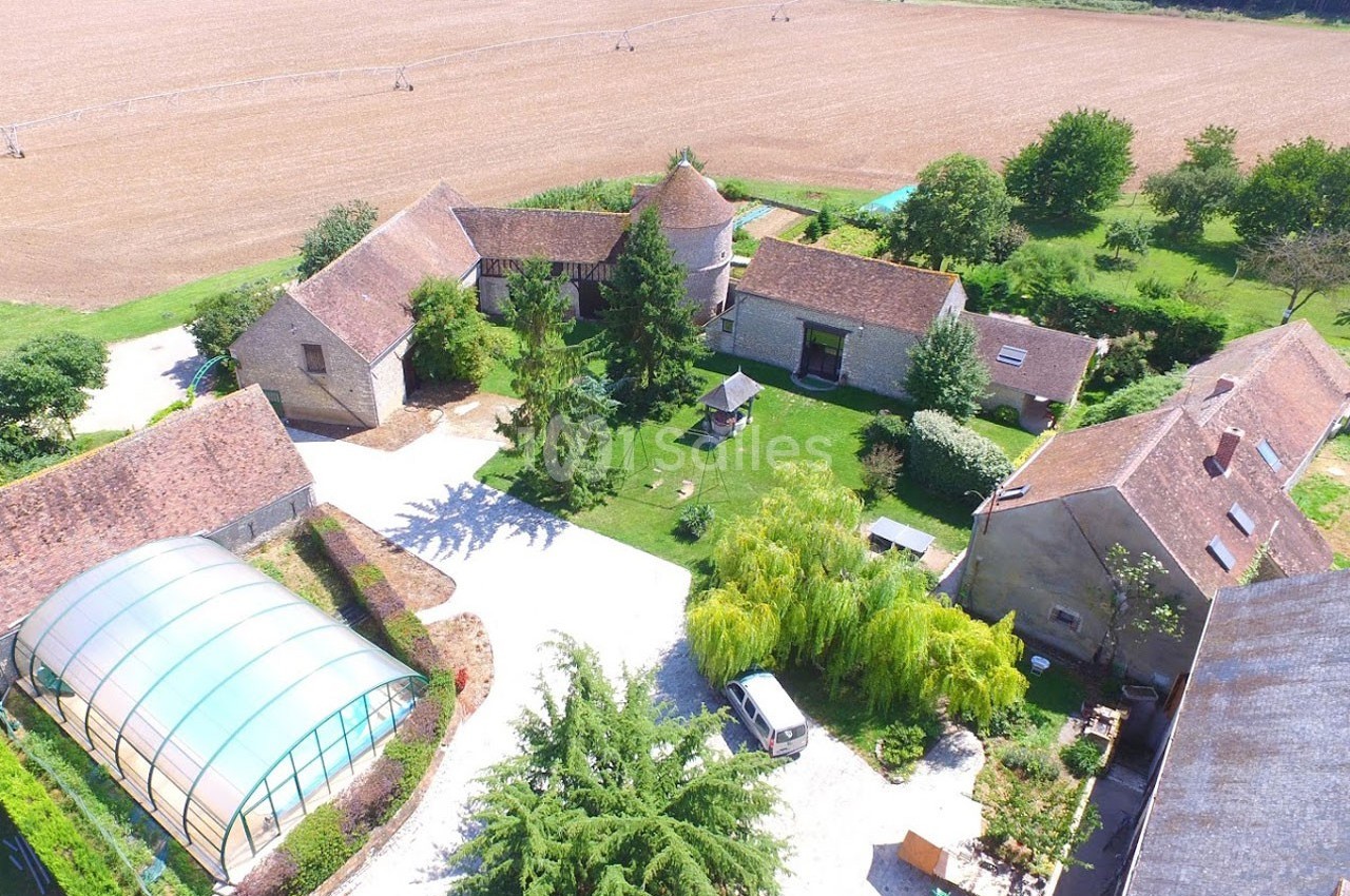 Vue aérienne d'un domaine rural avec bâtiments en pierre, cour centrale, serre et champs environnants.