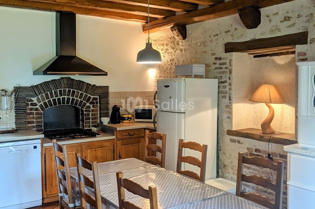 Cuisine rustique avec table en bois, électroménagers modernes, hotte en briques et lampe sur une niche murale.