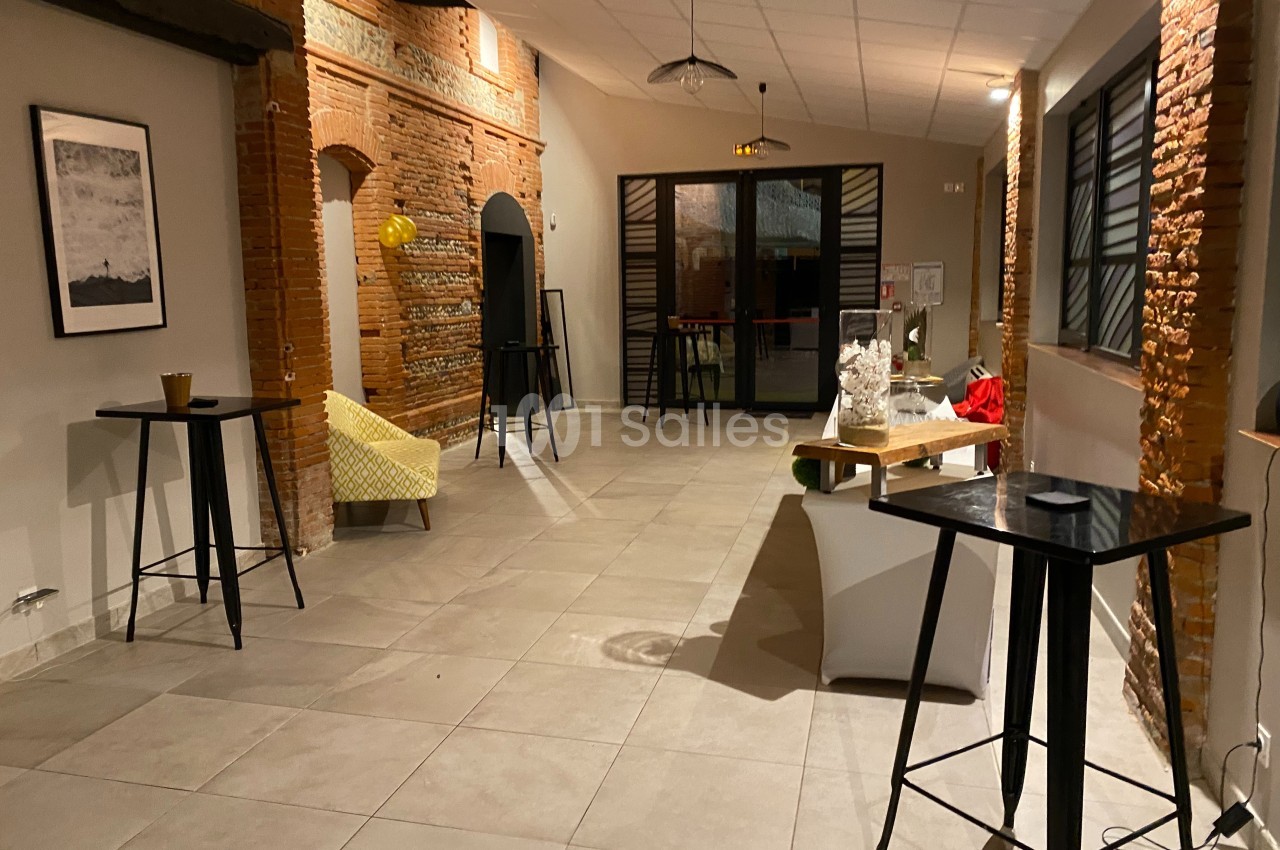 Salle lumineuse avec murs en briques, tables hautes, fauteuil jaune et décorations minimalistes.