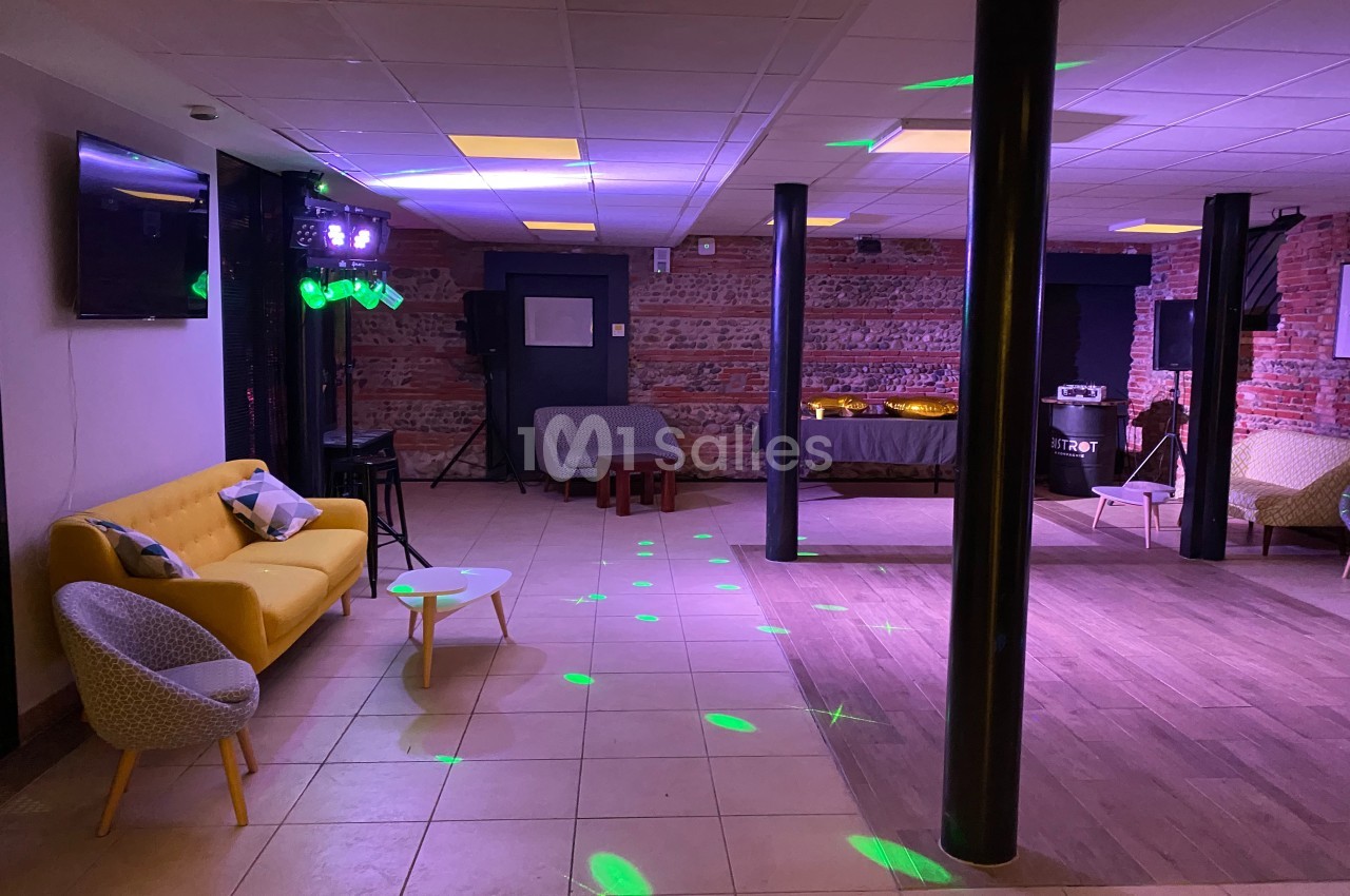 Salle avec un espace carrelé et parqueté, canapé jaune, tables basses, éclairages colorés et murs en briques.