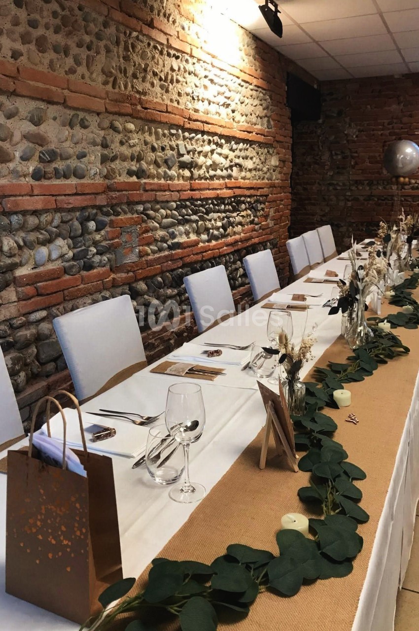 Table décorée pour un événement, avec nappes blanches, chemin de table en jute, feuillage et décorations élégantes.