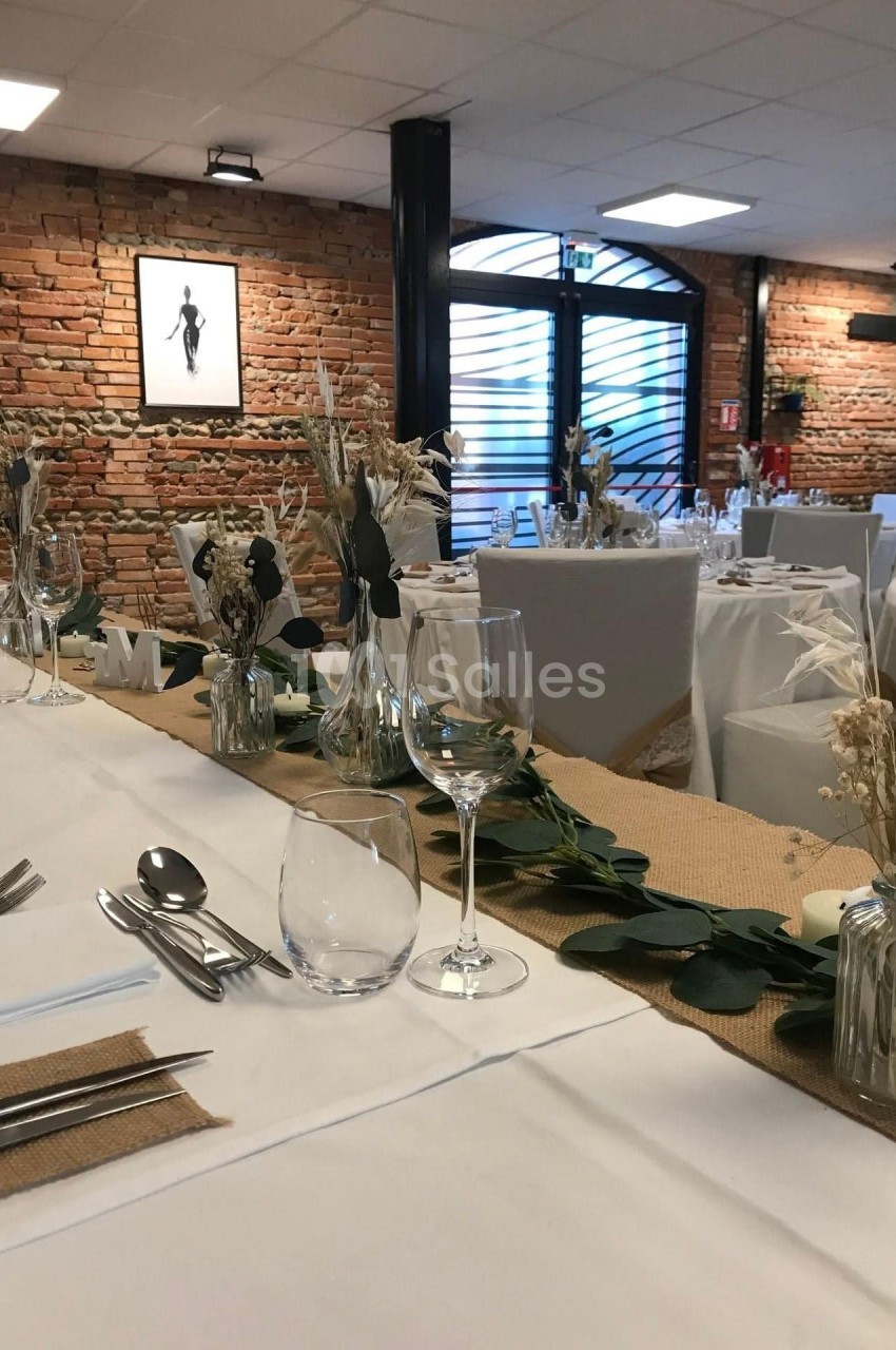Salle de réception décorée avec des tables dressées, ornées de fleurs séchées et de chemins de table en jute.