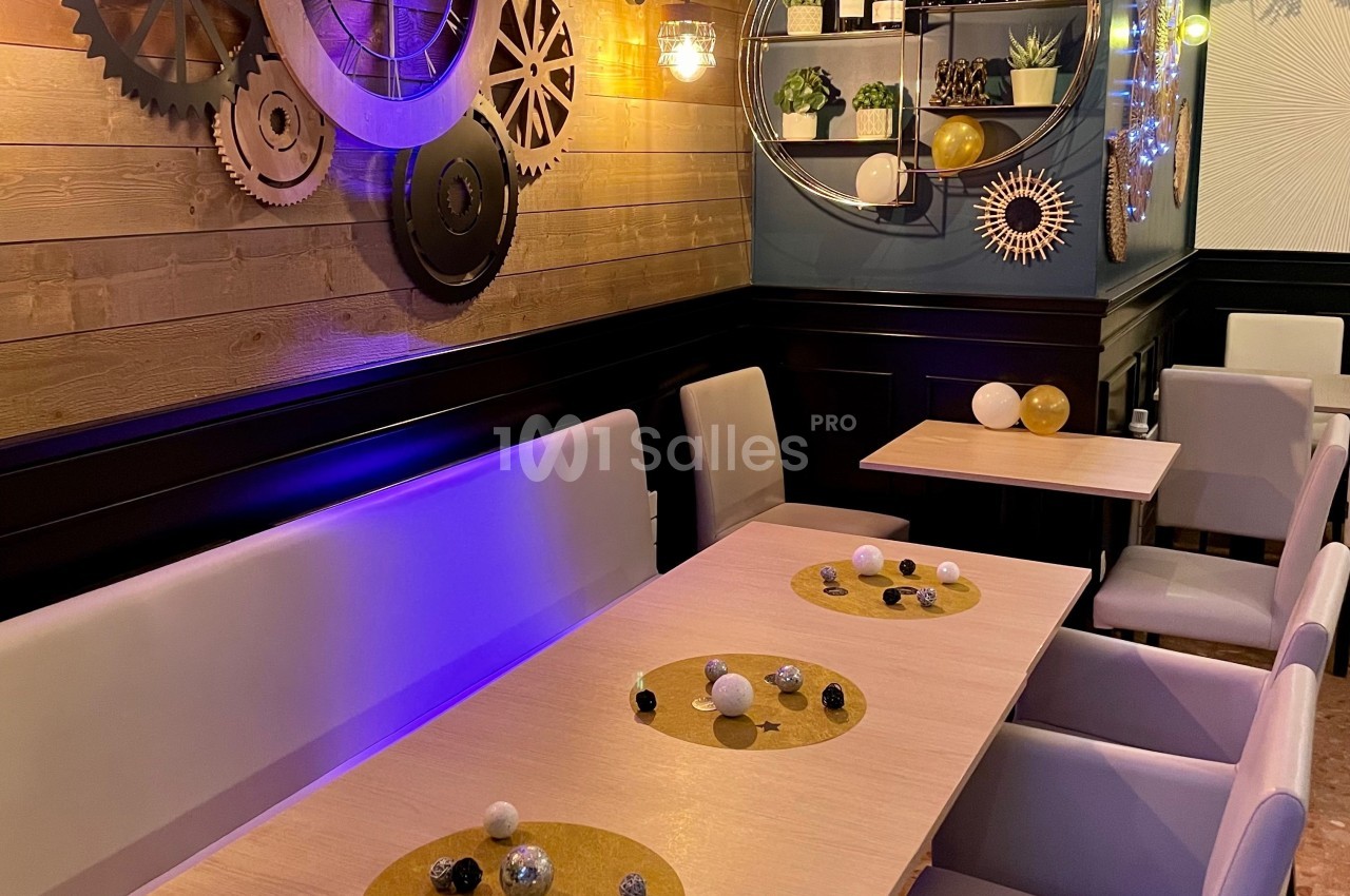 Salle de restaurant décorée avec des engrenages muraux, des plantes et des tables dressées avec des éléments décoratifs.