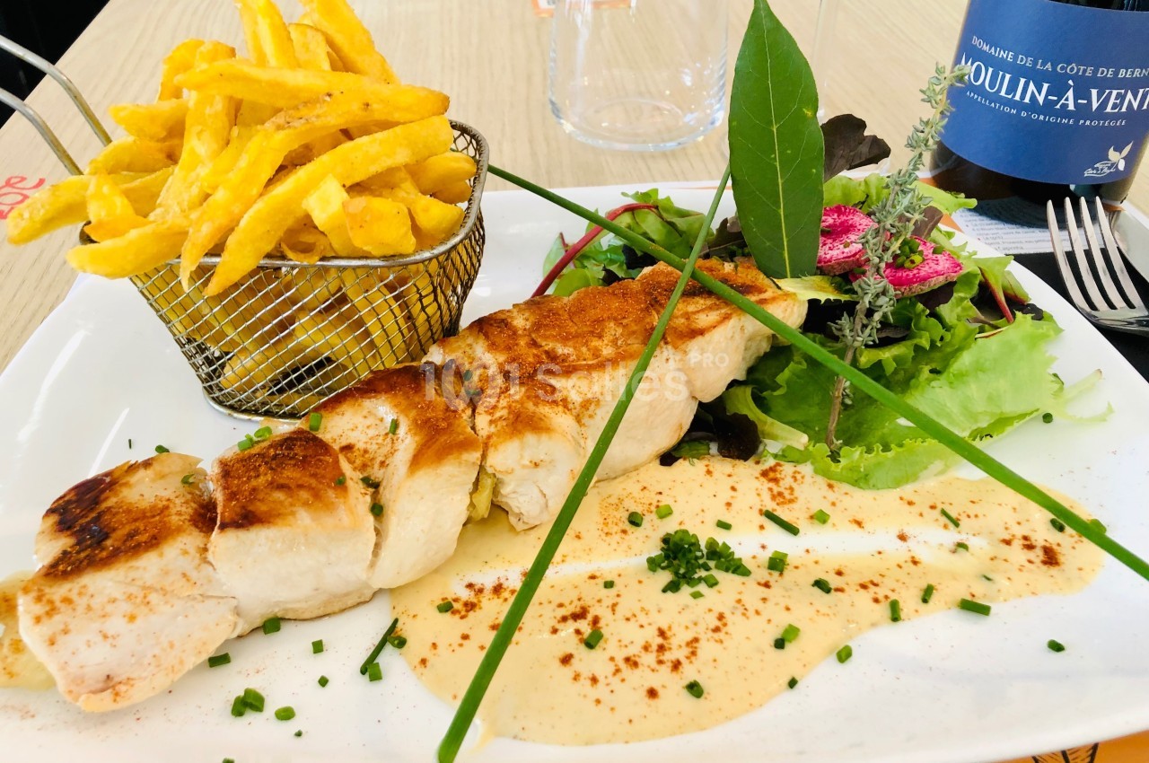 Assiette composée d'une brochette de poulet, frites dans un panier, salade verte et sauce, avec une bouteille de vin en…