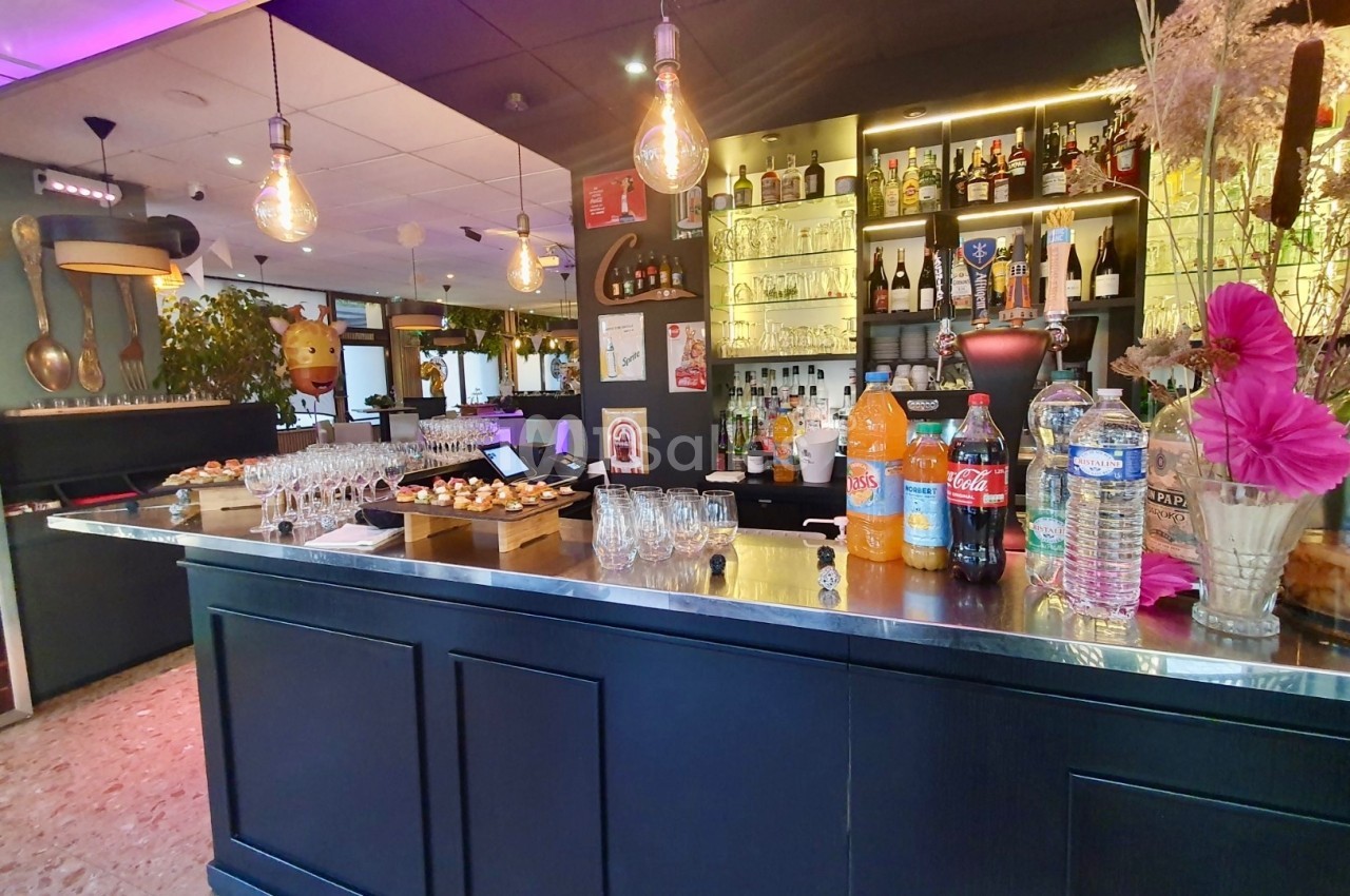 Comptoir de bar avec boissons, verres, amuse-bouches et étagères remplies de bouteilles en arrière-plan.