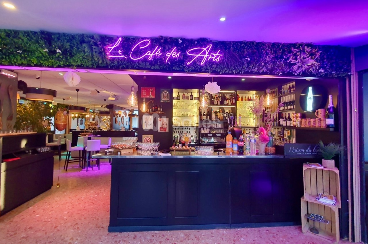 Intérieur d'un café avec un bar éclairé, des étagères remplies de bouteilles et une enseigne lumineuse au mur.