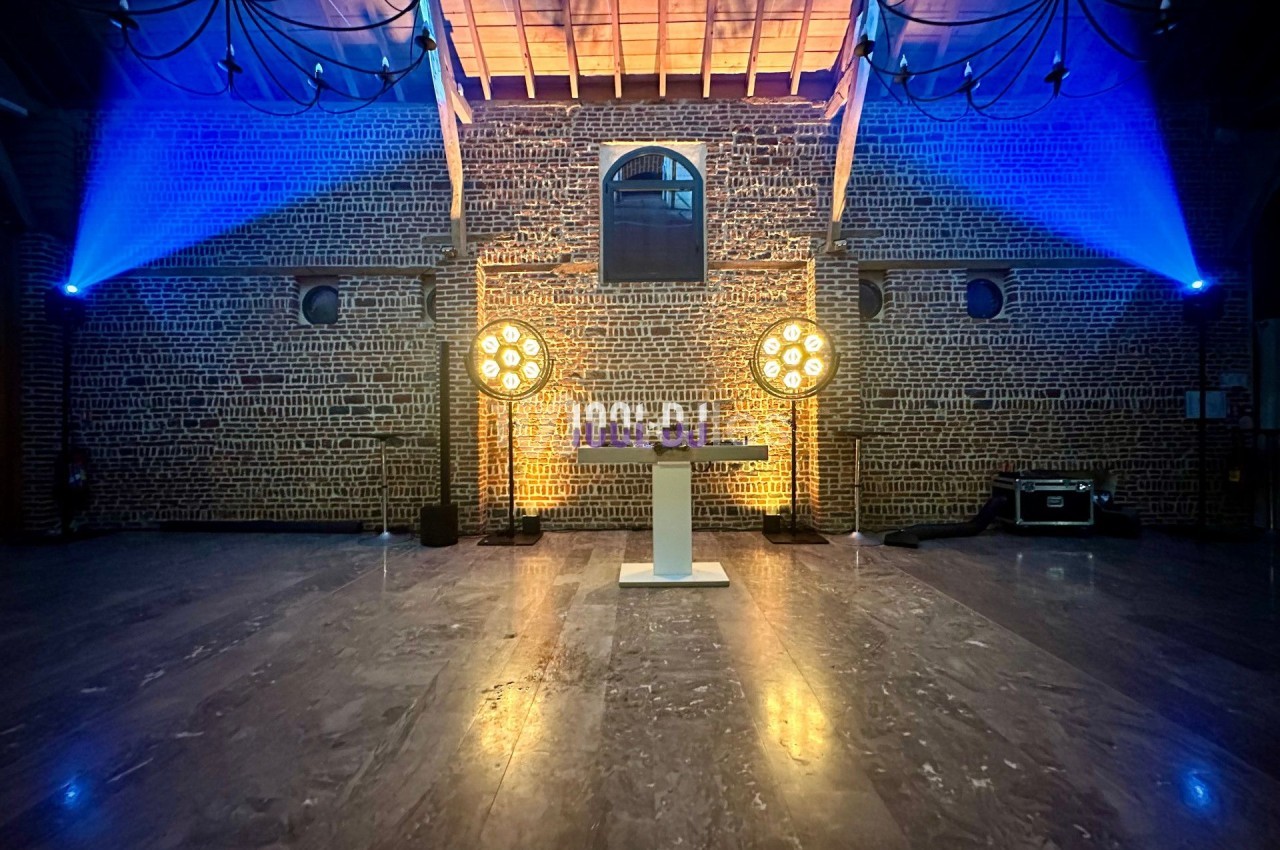 Salle en briques avec éclairage coloré, projecteurs circulaires et une table blanche au centre.