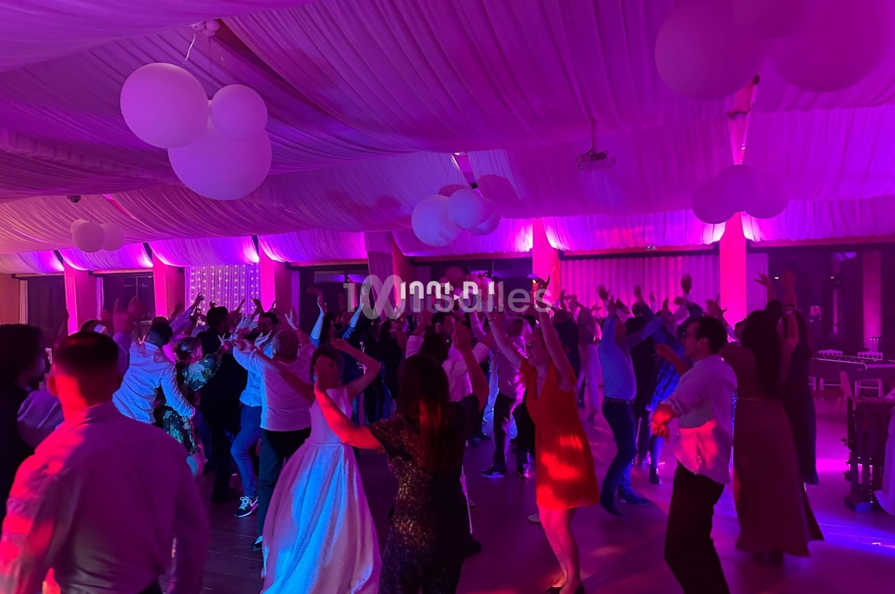 Des invités dansent sous un éclairage coloré dans une salle décorée avec des ballons suspendus et un plafond drapé.