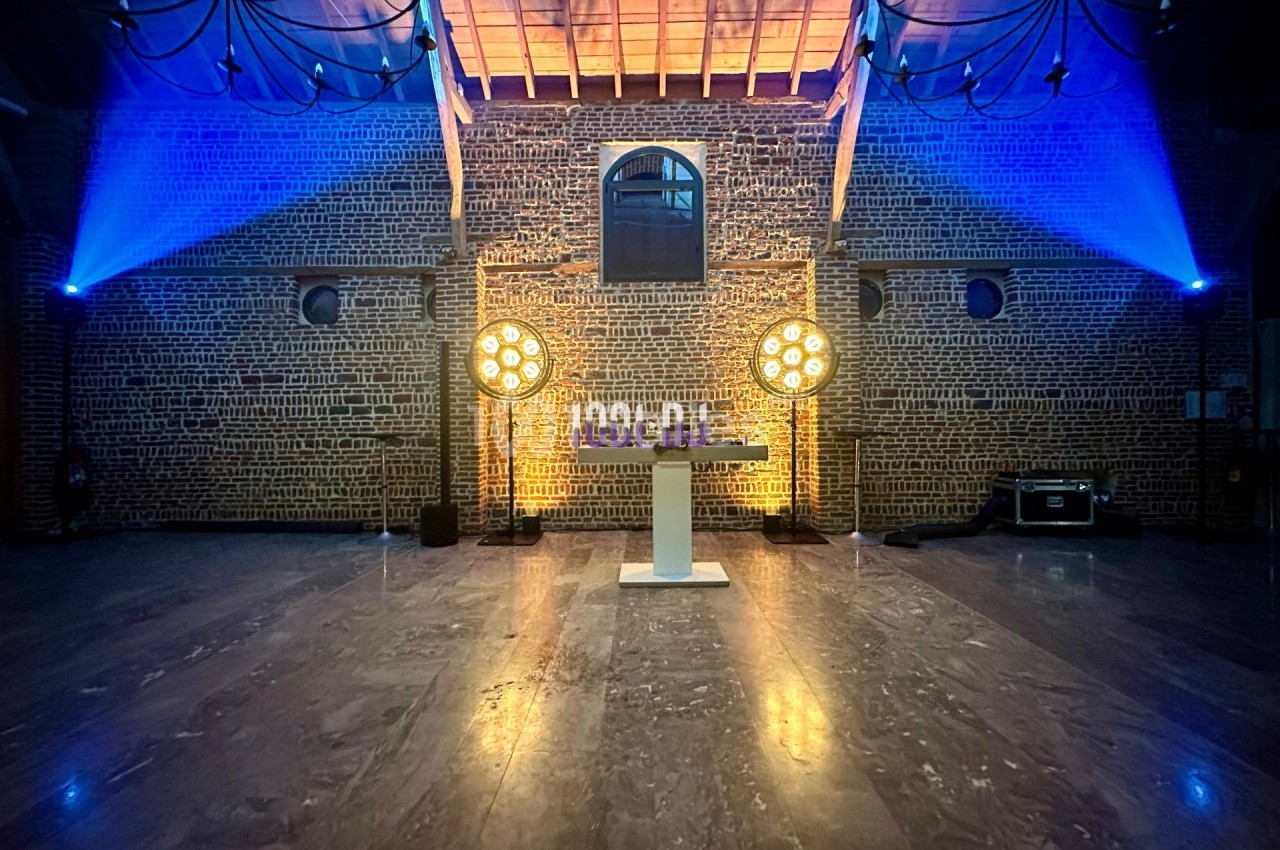 Salle en briques avec éclairage coloré, projecteurs circulaires et une table blanche au centre.