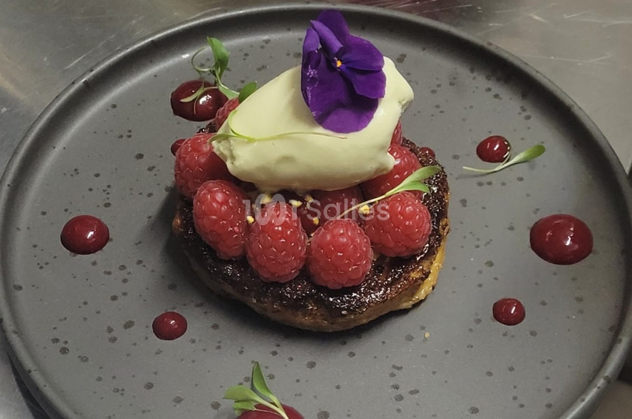 Dessert composé de framboises fraîches, glace vanille, fleur comestible violette, sur une base caramélisée.