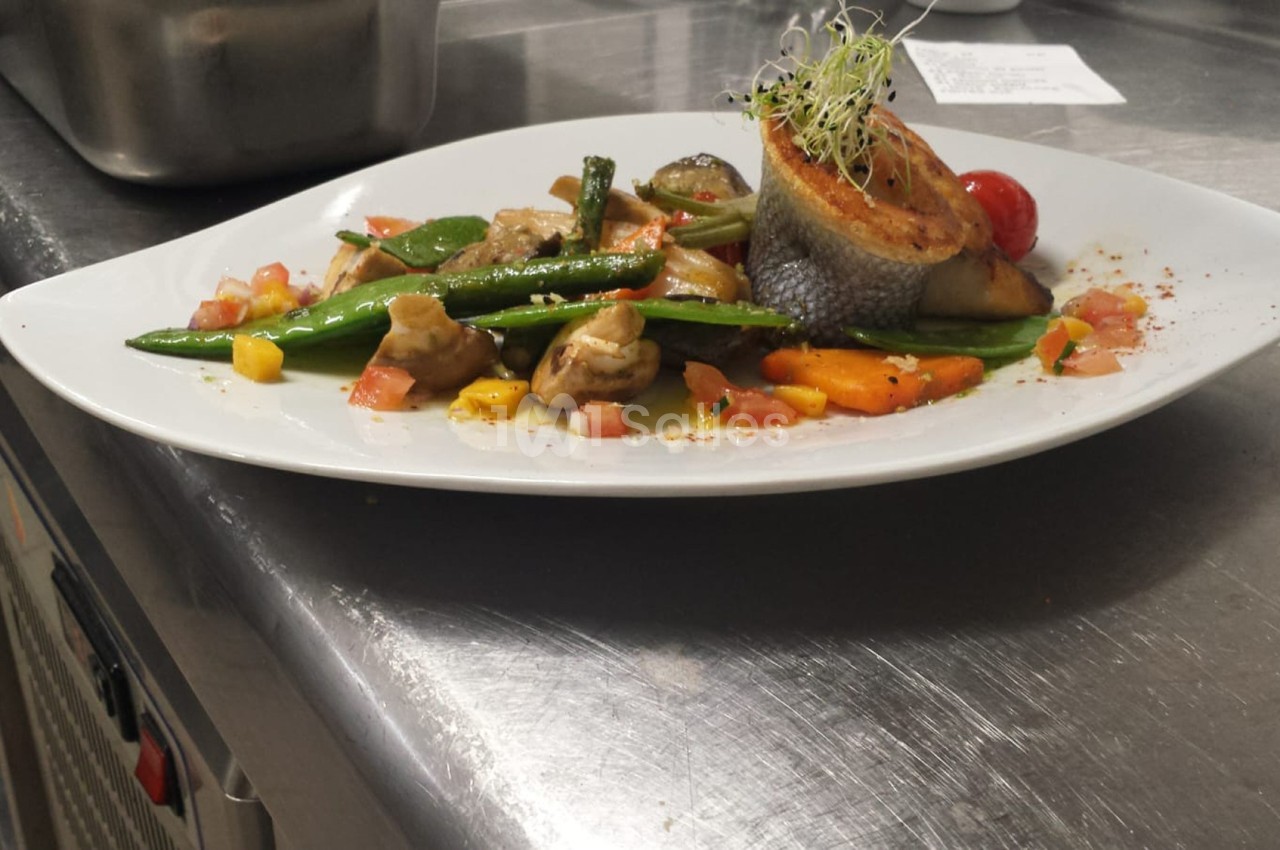 Assiette de poisson grillé accompagné de légumes colorés et garnie de jeunes pousses, servie sur une table en inox.