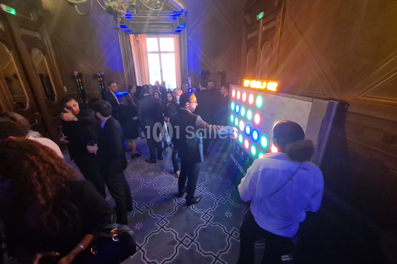 Personnes rassemblées dans une salle élégante, certaines interagissant avec un mur lumineux coloré.