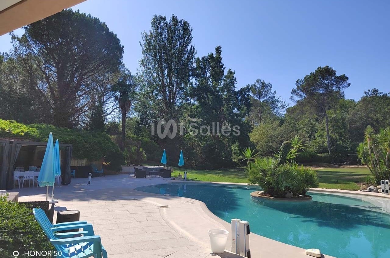 Piscine extérieure bordée de chaises et parasols bleus, entourée de végétation dense et d'arbres.