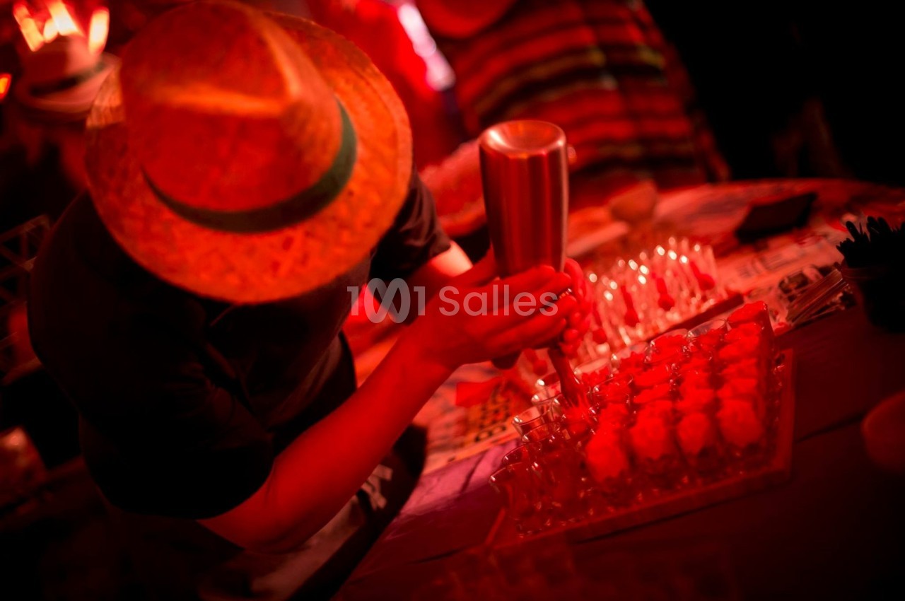 Un homme portant un chapeau prépare des desserts rouges avec une poche à douille dans un environnement éclairé en rouge.