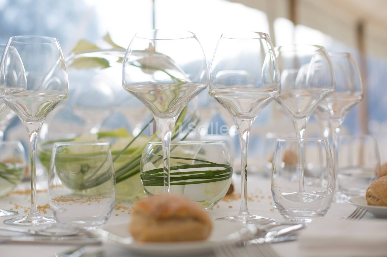 Table dressée avec des verres en cristal, des assiettes, un pain individuel et une décoration végétale élégante.