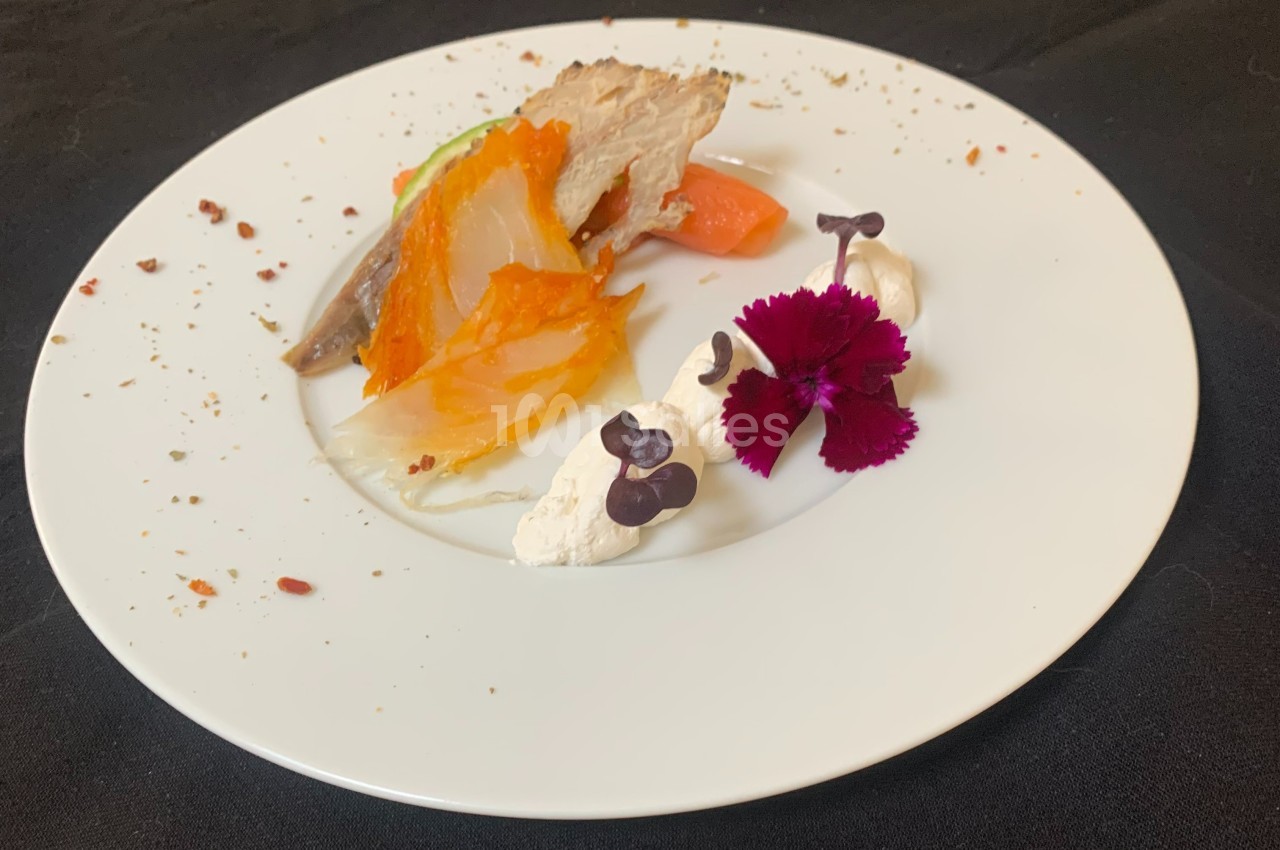 Assiette gastronomique avec légumes colorés, crème, fleurs comestibles et morceau de viande, présentée sur une nappe noire.