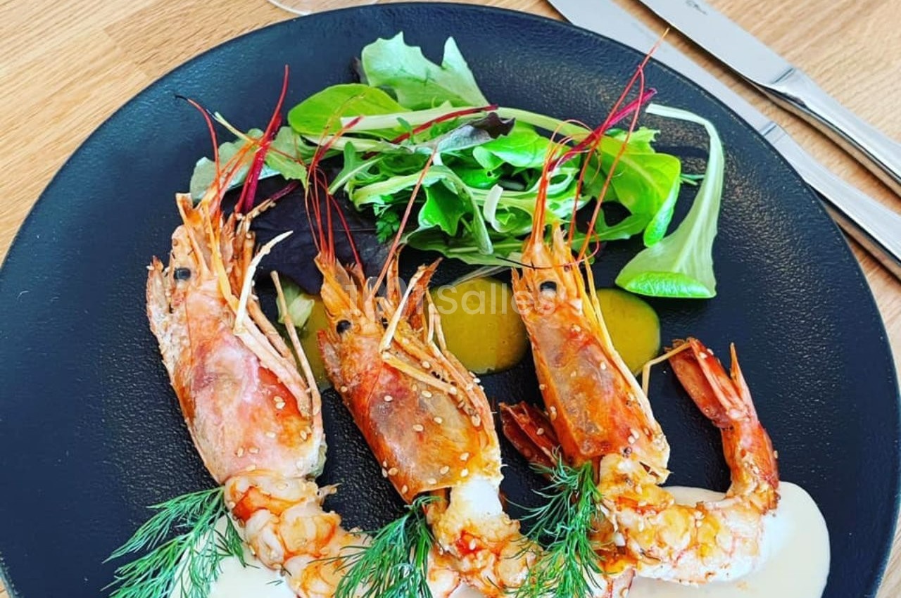 Assiette contenant trois gambas grillées, accompagnées de sauce, d'herbes fraîches et de salade verte.