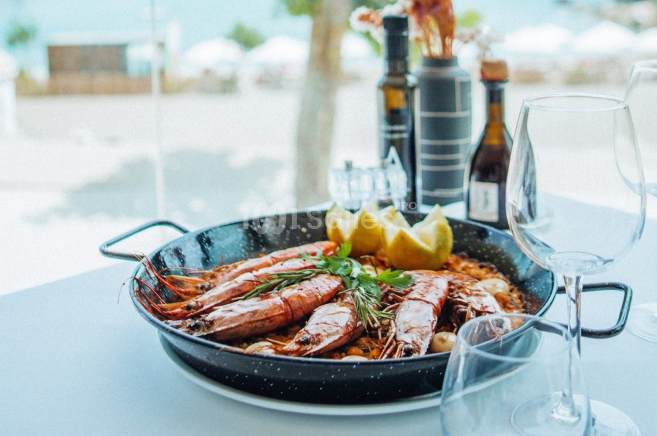 Plat de crevettes grillées servi avec des herbes et des quartiers de citron, posé sur une table en extérieur près de la mer.