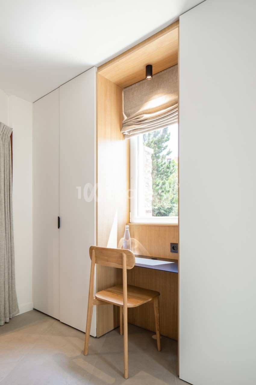 Coin bureau minimaliste avec une chaise en bois, un bureau intégré près d'une fenêtre et des rangements encastrés.