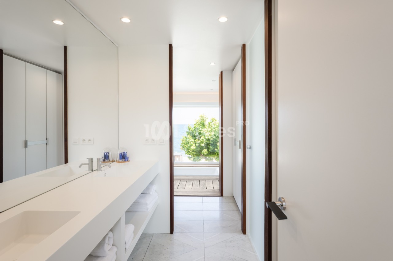 Salle de bain moderne avec lavabo blanc, grande glace, et vue sur une terrasse donnant sur un paysage extérieur lumineux.