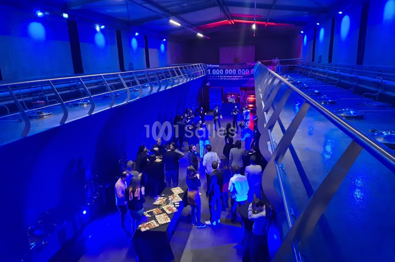 Salle moderne éclairée de lumières bleues, avec des groupes de personnes discutant près de tables et d'expositions.