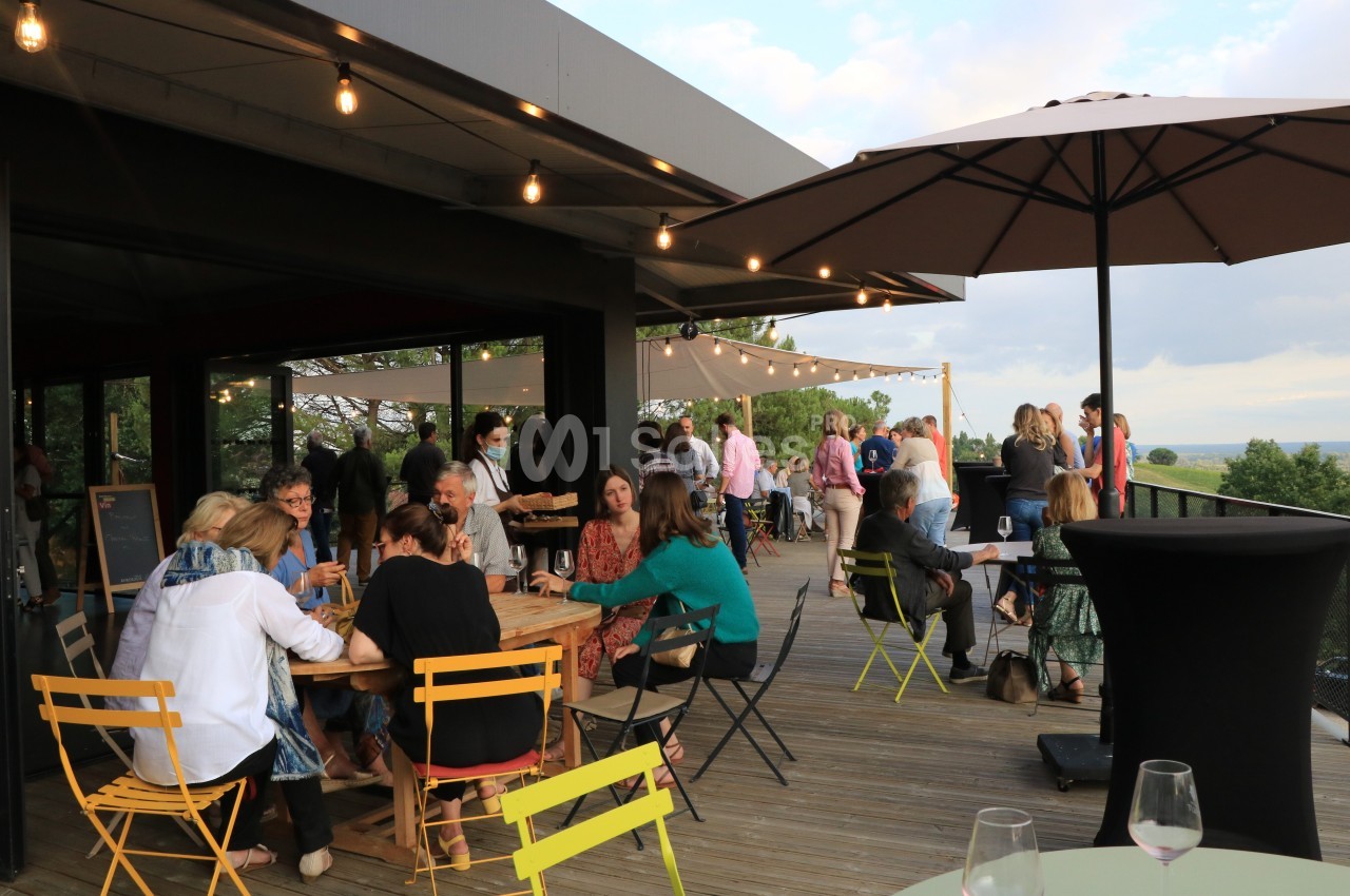 Personnes réunies sur une terrasse en bois, discutant et partageant un moment convivial sous des guirlandes lumineuses.