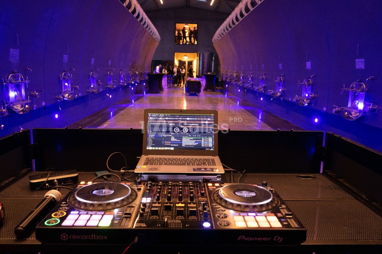 Table de mixage DJ avec ordinateur portable dans une salle moderne éclairée de lumières violettes, avec des invités au fond.