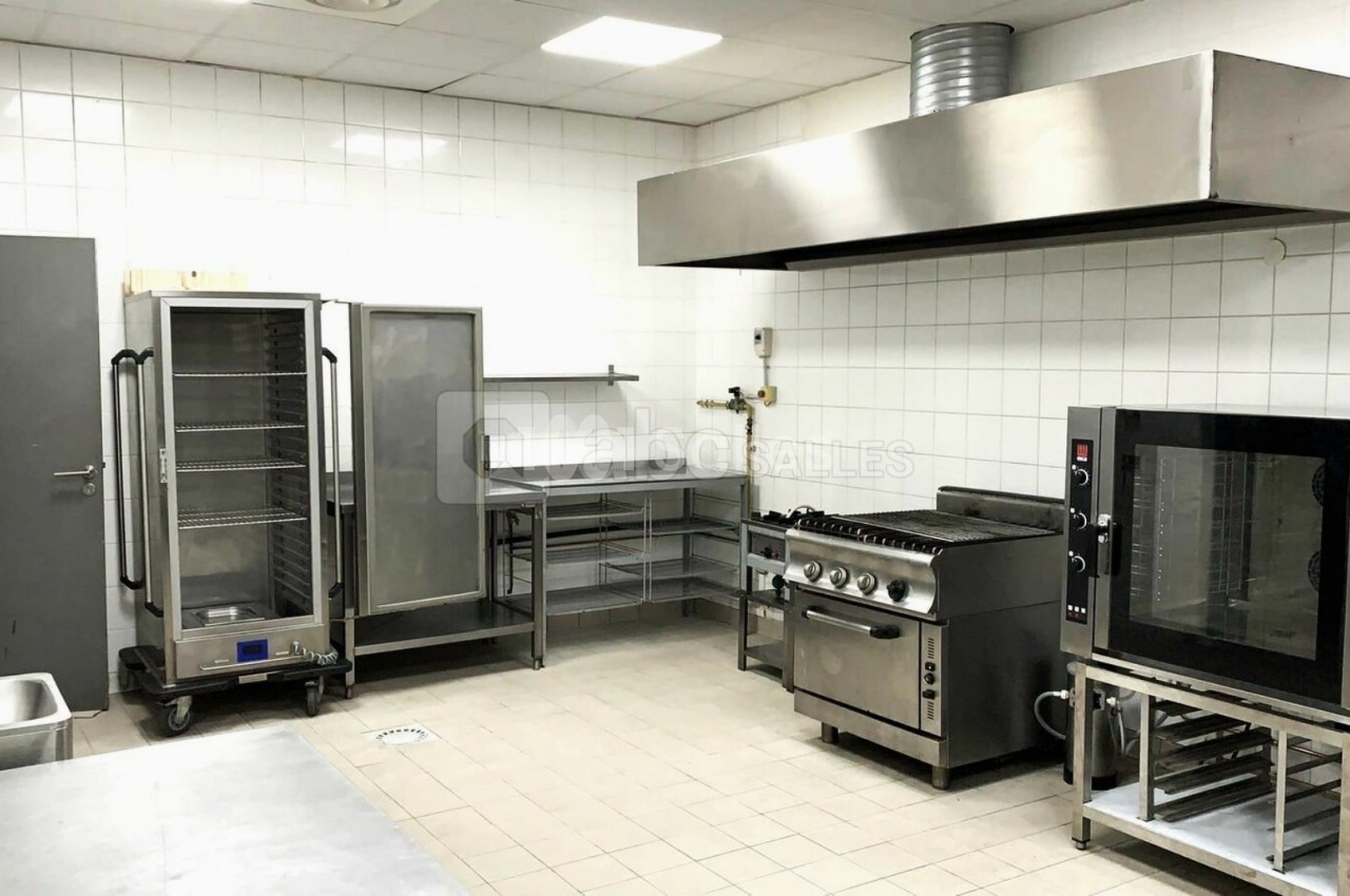 Cuisine professionnelle équipée avec four, réfrigérateur, plan de travail en inox et hotte d'extraction.