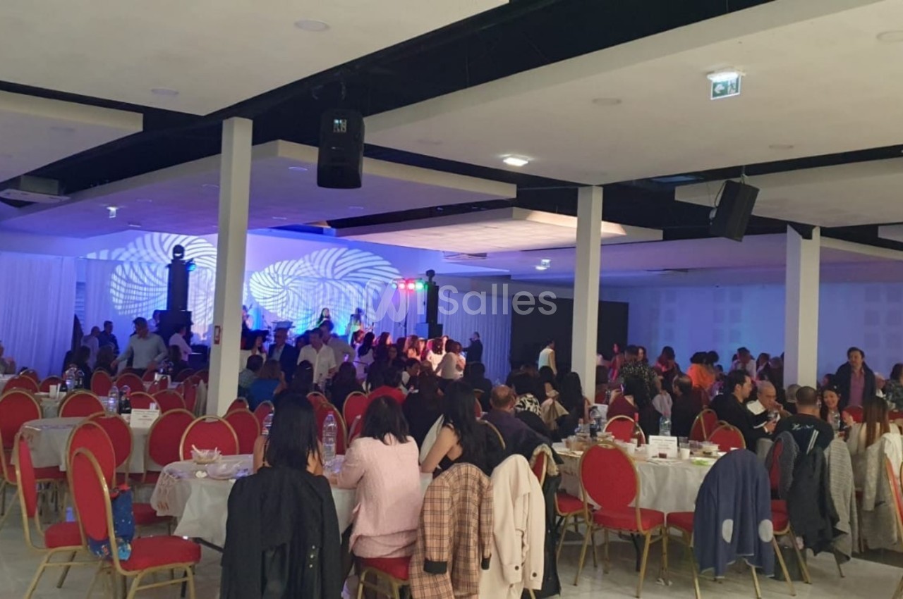 Salle de réception avec des invités assis à des tables rondes et une scène éclairée en arrière-plan.