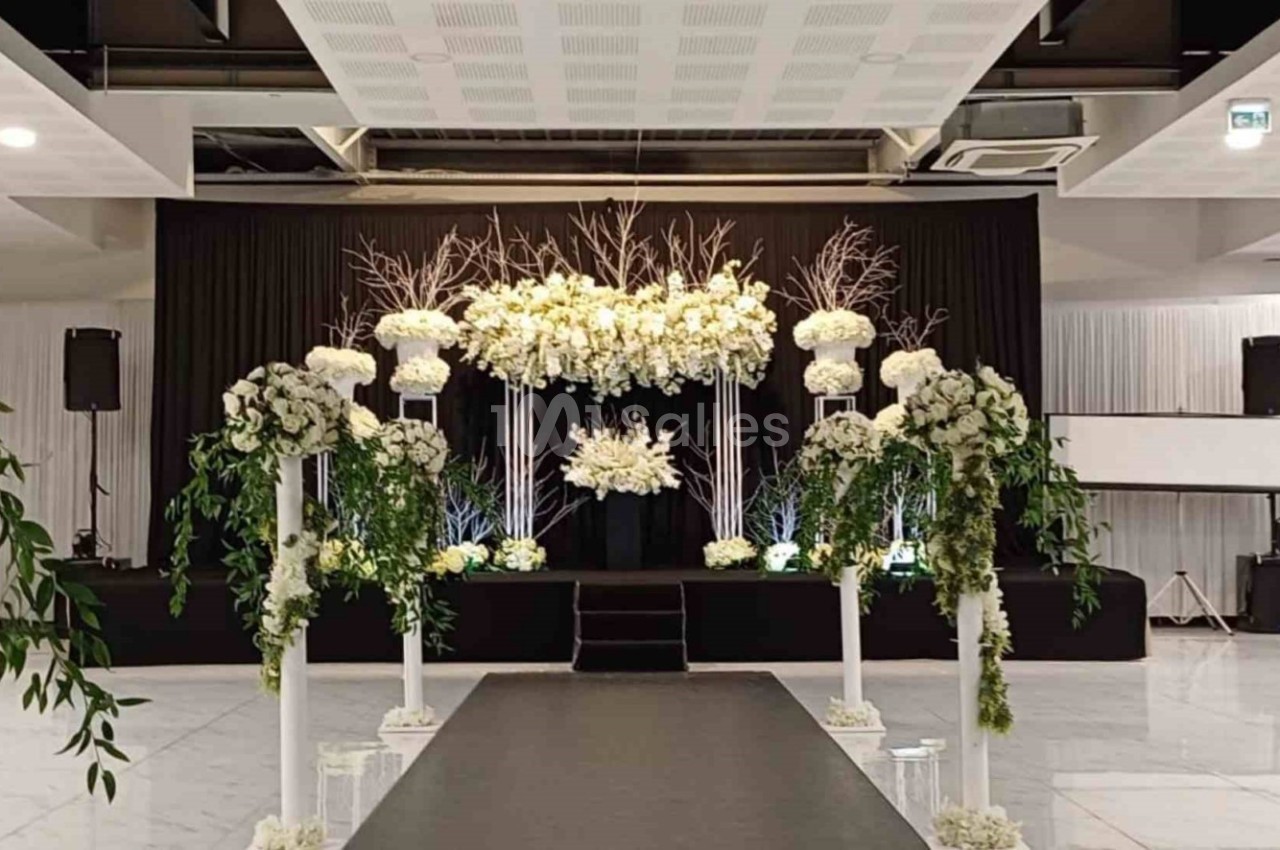 Allée décorée de fleurs blanches et verdure menant à une scène ornée d'arrangements floraux dans une salle de réception.