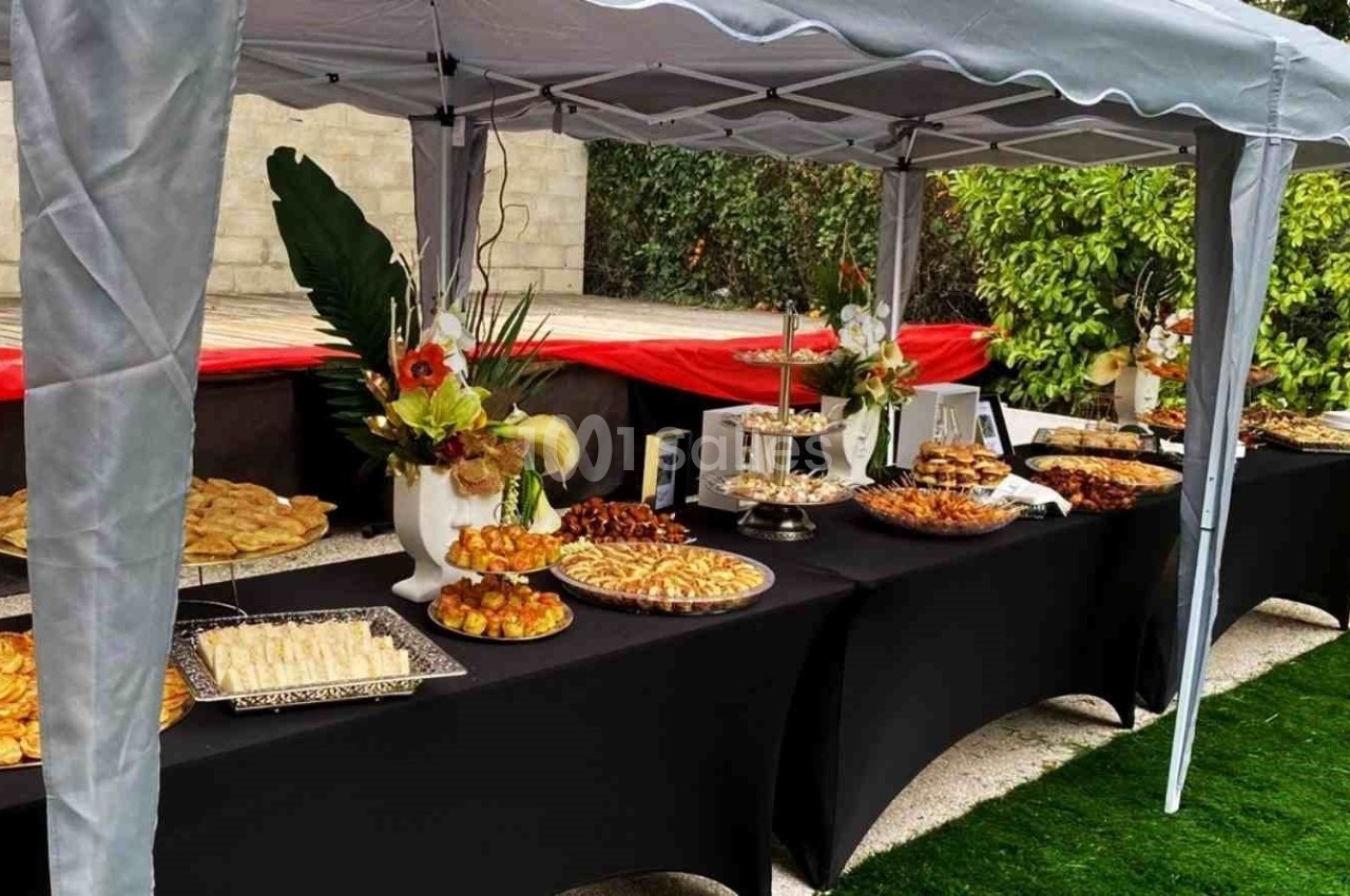 Buffet varié disposé sous une tente, avec des plats salés et sucrés présentés sur des tables noires en extérieur.
