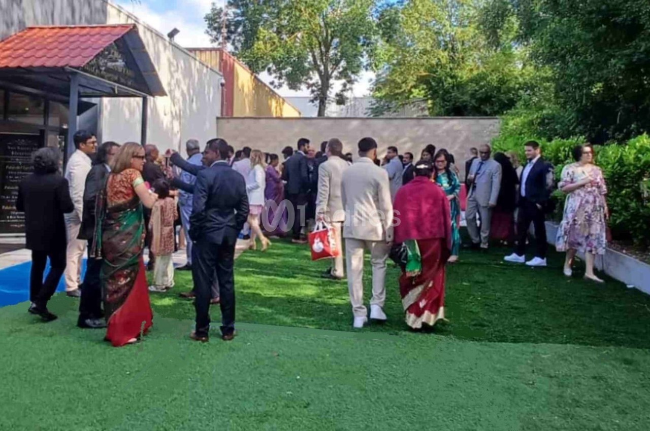 Un groupe de personnes en tenue habillée discute dans un jardin extérieur près d'un bâtiment moderne.