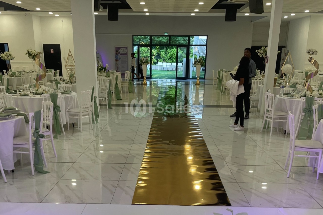 Salle de réception décorée avec des tables rondes, nappes blanches, chaises assorties et une allée centrale dorée.