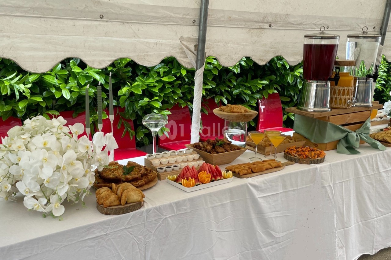 Buffet sous une tente avec viennoiseries, fruits, plats salés et boissons disposés sur une table blanche.