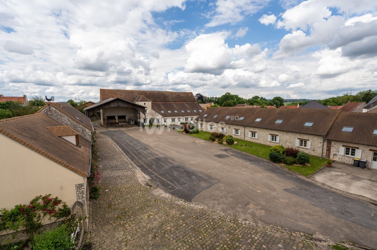 Cour pavée entourée de bâtiments en pierre avec toits en tuiles, sous un ciel partiellement nuageux.