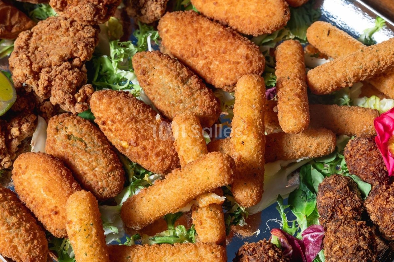 Assortiment de snacks frits, dont bâtonnets de mozzarella, nuggets et falafels, disposés sur un lit de salade.