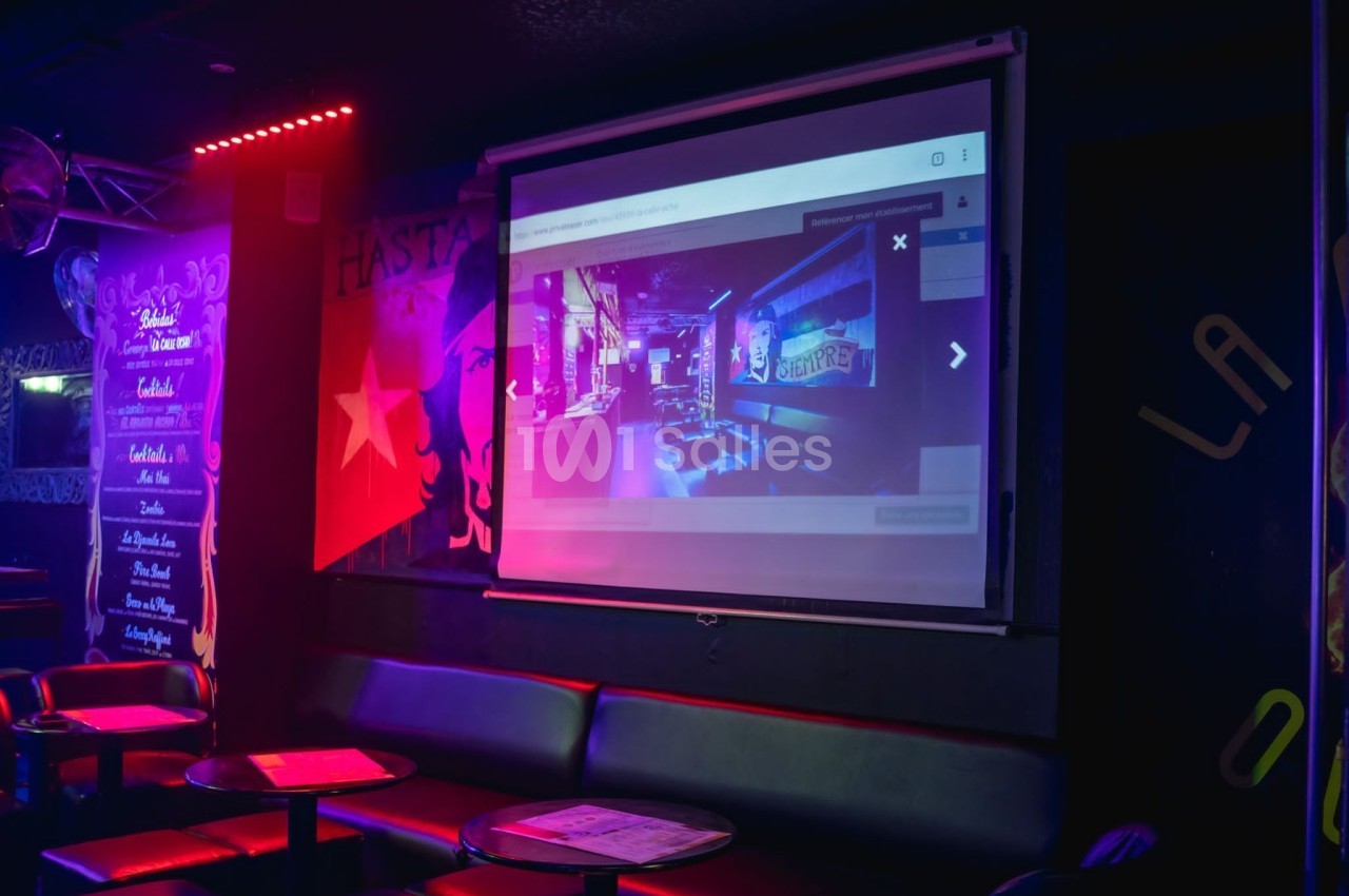 Écran de projection affichant une image d'intérieur coloré dans un espace sombre avec sièges et éclairage néon.