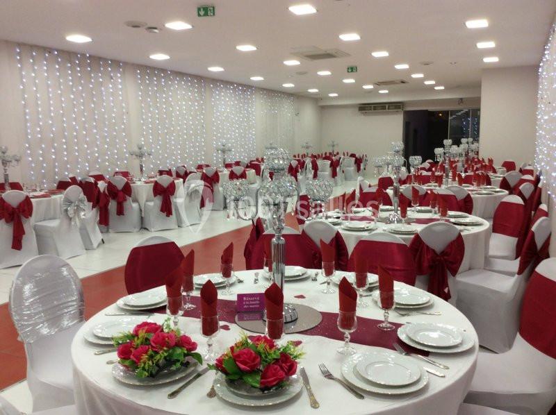 Salle de réception décorée avec des nappes blanches, des nœuds rouges sur les chaises et des tables dressées élégamment.