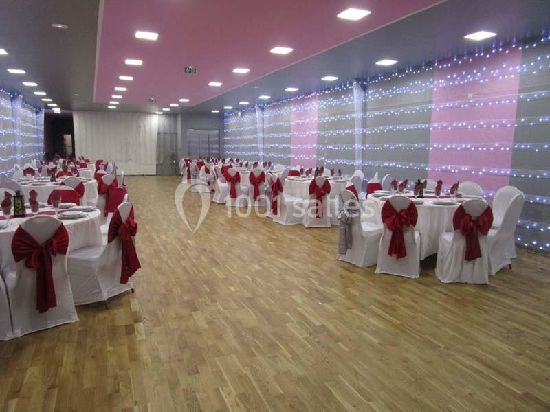 Salle de réception décorée avec des chaises blanches ornées de nœuds rouges et des guirlandes lumineuses sur les murs.