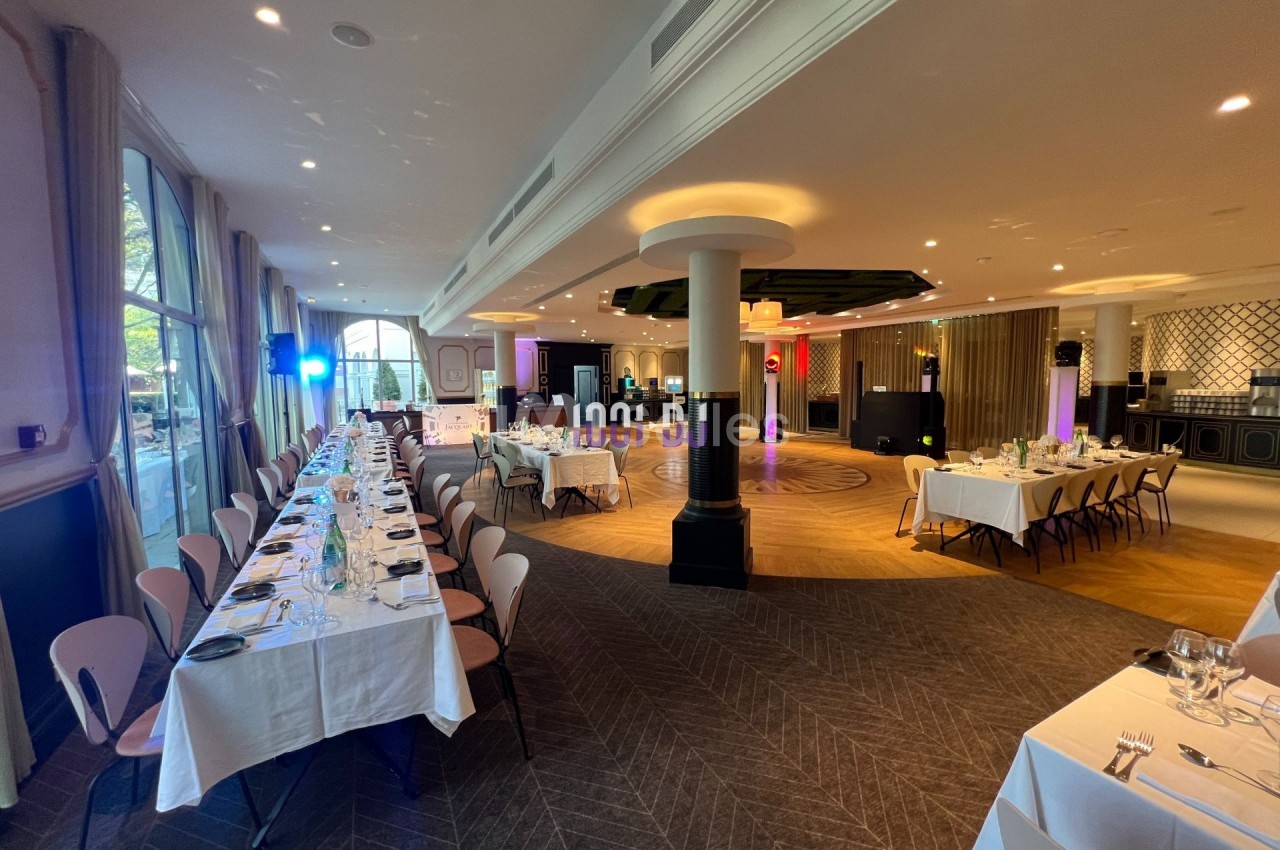 Salle de réception élégante avec tables dressées, éclairages colorés et espace central dégagé.