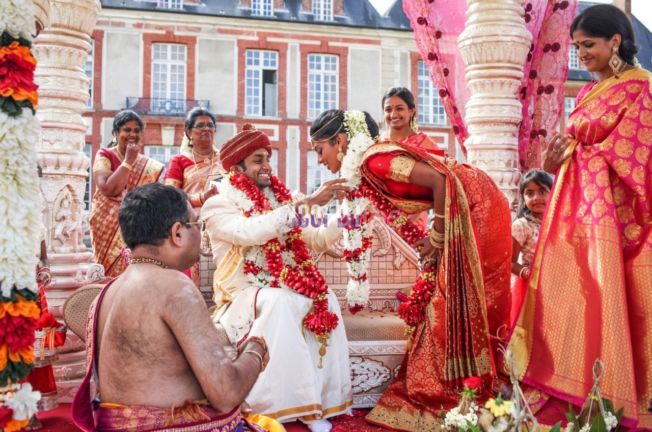Un couple en tenue traditionnelle indienne échange des guirlandes lors d'une cérémonie de mariage en extérieur.