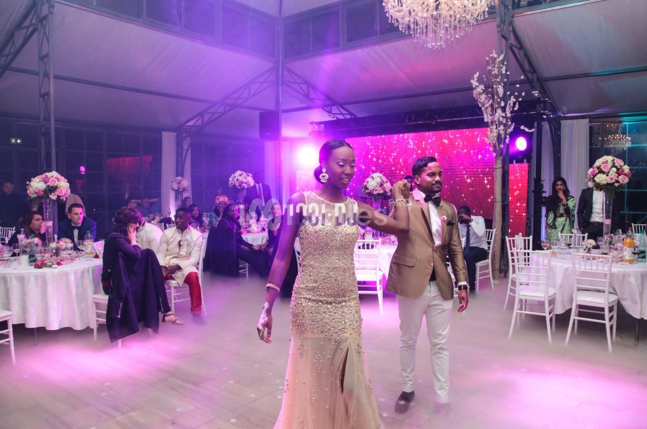 Un couple danse au centre d'une salle de réception décorée avec des fleurs et éclairée par des lumières colorées.